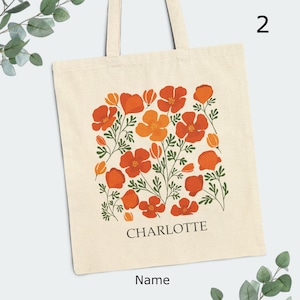 May include: A white canvas tote bag with a floral design featuring orange and red poppy flowers. The bag has a black text that says "CHARLOTTE" and "Name" below the design.