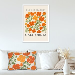 Pu&ograve; includere: Una stampa artistica incorniciata e un cuscino decorativo con un design floreale. La stampa recita "Flower Market California" con papaveri arancioni e foglie verdi. Il cuscino ha un motivo simile di fiori arancioni e foglie verdi.