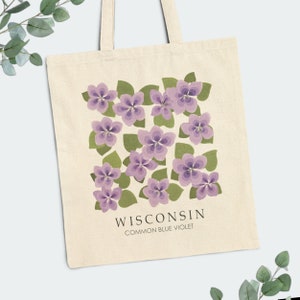 May include: A white tote bag with a design of purple flowers and green leaves. The text "WISCONSIN COMMON BLUE VIOLET" is printed below the design.