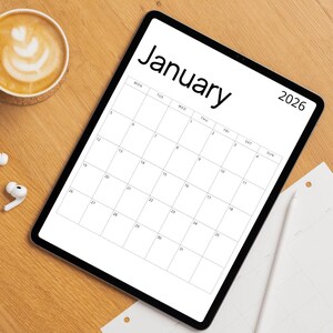 May include: A digital tablet displaying a January 2026 calendar in black and white. The word "January" is at the top, with the year 2026 on the right. A cup of coffee and earbuds are on the wooden surface.