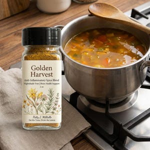 以下が含まれることがあります： 黒い蓋が付いた「Golden Harvest」スパイスブレンドのガラス瓶が、コンロの上のスープが入った鍋の隣にあります。瓶のラベルには、抗炎症特性と花のイラストに関するテキストが含まれています。木のスプーンがスープの中にあります。