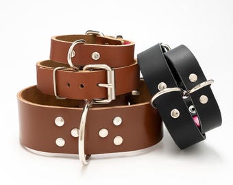 Puede incluir: Tres collares de perro de cuero, uno negro y dos marrones. Los collares marrones tienen hebillas y tachuelas plateadas. El collar negro tiene una hebilla plateada.