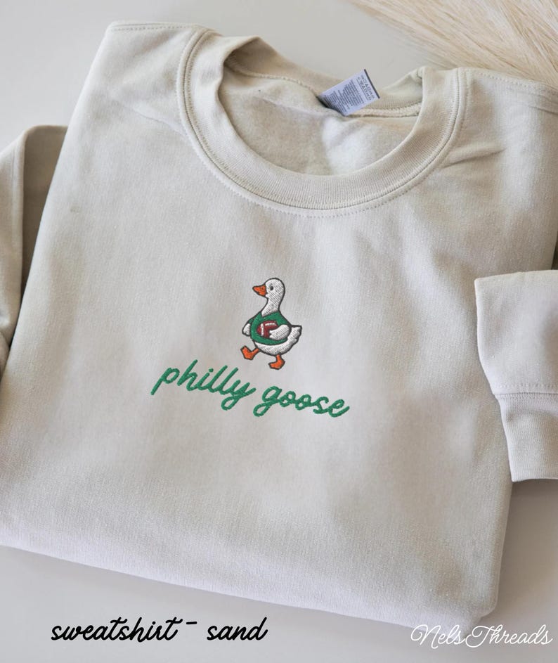 May include: A sand-colored crewneck sweatshirt featuring an embroidered graphic of a white goose wearing a green jersey and holding a brown football. Below the goose, the text "philly goose" is embroidered in green cursive script lettering.
Philadelphia Football, Embroidered Crewneck Sweatshirt, T-Shirt Embroidery, Philly Goose, Silly Goose
philly goose philly goose sweatshirt philadelphia philly goose shirt retro philadelphia designs philly crewneck