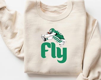 May include: A cream-colored sweatshirt with a green graphic of a football player jumping and the word "Fly" in green letters.