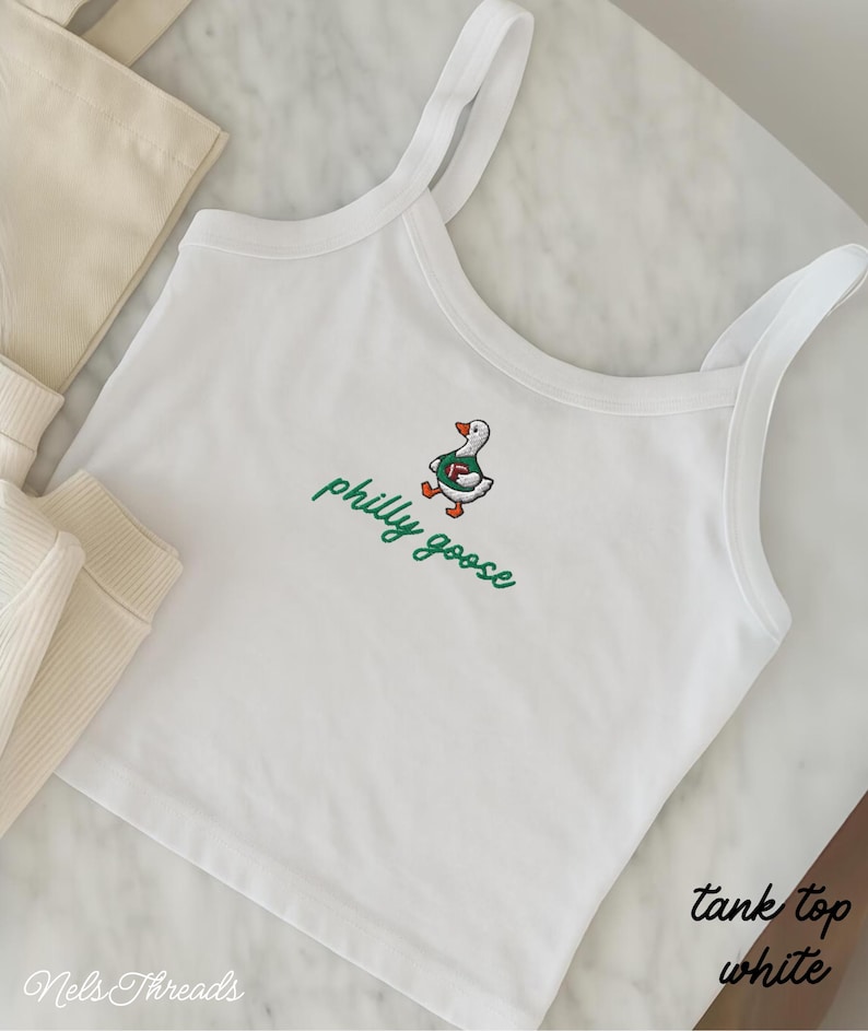 May include: A white tank top featuring an embroidered graphic of a goose wearing a green jersey and holding a football, with the text philly goose in green cursive script below the goose. The garment has thin shoulder straps and a scoop neckline.
Philadelphia Football, Embroidered Crewneck Sweatshirt, T-Shirt Embroidery, Philly Goose, Silly Goose
philly goose philly goose sweatshirt philadelphia philly goose shirt retro philadelphia designs philly crewneck tank top spaghetti straps white tank