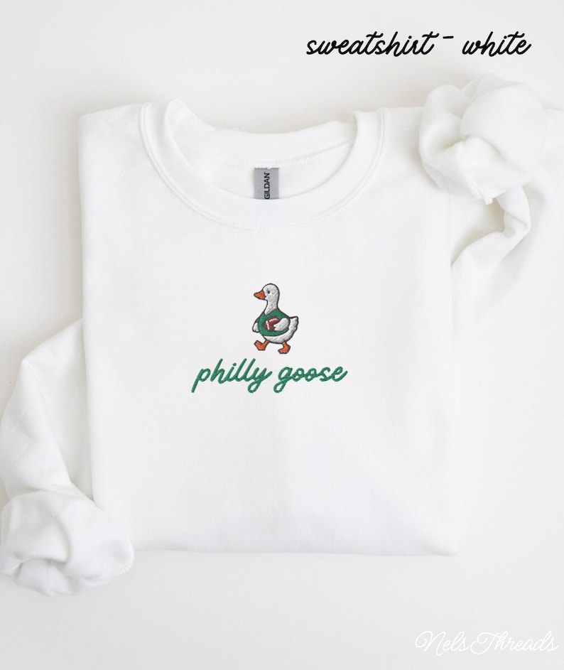 May include: A white crewneck sweatshirt featuring an embroidered graphic of a goose wearing a green jersey and holding a football. Below the goose, the text philly goose is embroidered in green script. The text sweatshirt - white appears at the top.
Philadelphia Football, Embroidered Crewneck Sweatshirt, T-Shirt Embroidery, Philly Goose, Silly Goose
philly goose philly goose sweatshirt philadelphia philly goose shirt retro philadelphia designs philly crewneck
