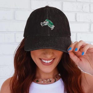 May include: Black denim baseball cap with an embroidered green and white football player design. The cap has a curved brim and a classic six-panel construction. A stylish accessory for sports fans.