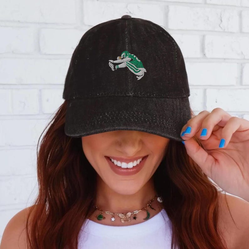 May include: Black denim baseball cap with an embroidered green and white football player design. The cap has a curved brim and a classic six-panel construction. A stylish accessory for sports fans.