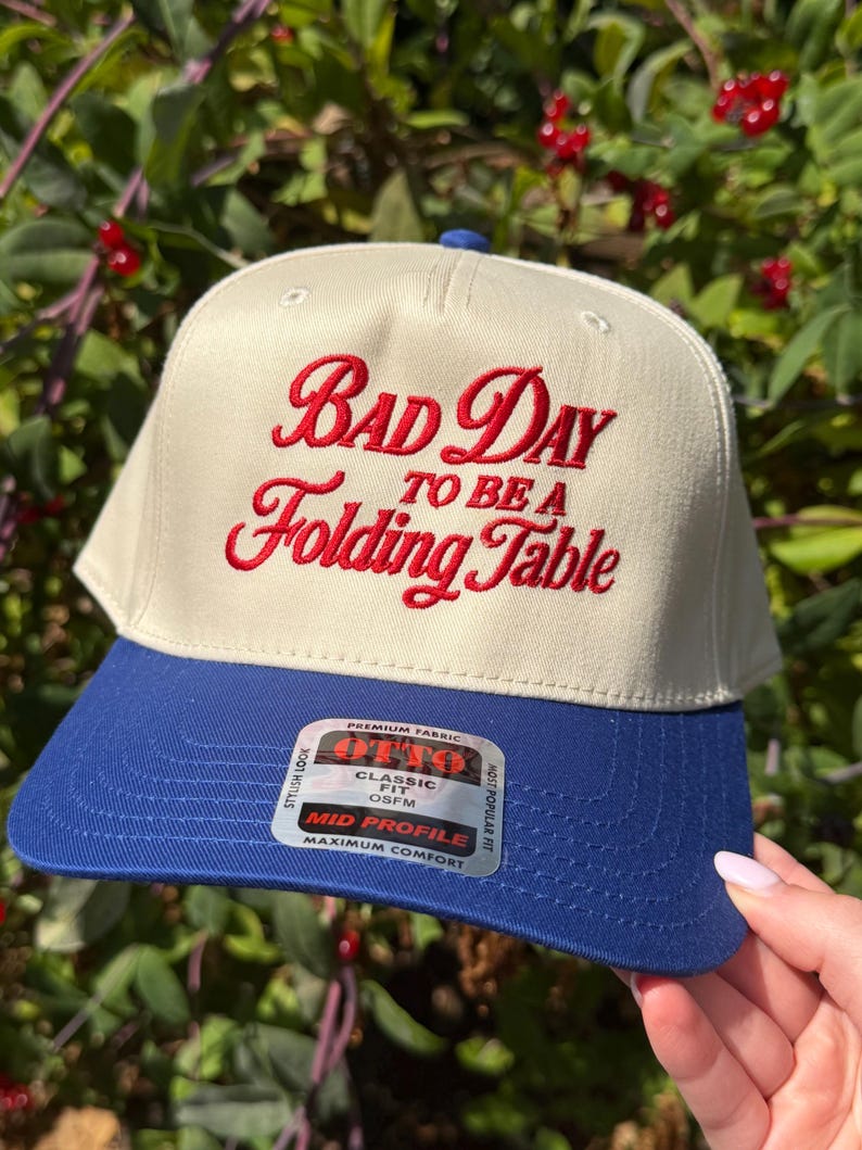 May include: A cream-colored baseball cap with a blue brim featuring red embroidered text that reads "BAD DAY TO BE A Folding Table". A rectangular sticker on the brim displays the brand name OTTO, the text "CLASSIC FIT OSFM", and "MID PROFILE".
buffalo hat embroidered hat funny hat buffalo apparel embroidery hat buffalo football funny football hat bad day to be a folding table hat women bad day table hat football trucker hat buffalo mens gifts buffalo apparel for him gift for her football him