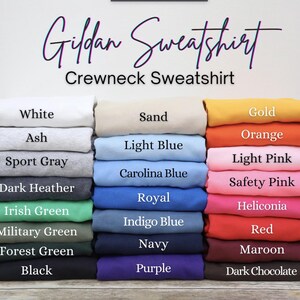 Op de afbeelding: Een stapel Gildan crewneck sweatshirts in diverse kleuren, waaronder wit, asgrijs, sportgrijs, donker heidegrijs, iers groen, militair groen, bosgroen, zwart, zand, lichtblauw, carolinablauw, koningsblauw, indigoblauw, marineblauw, paars, goud, oranje, lichtroze, veiligheidsroze, heliconia, rood, kastanjebruin en donkere chocolade.