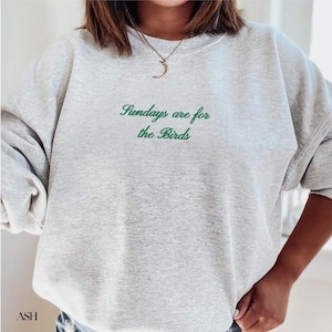 K&ouml;nnte beinhalten: Hellgraues Sweatshirt mit dem gr&uuml;nen Schriftzug "Sundays are for the Birds". Das Sweatshirt hat eine lockere Passform und lange &Auml;rmel. Das Wort "ASH" ist unten links aufgedruckt.
