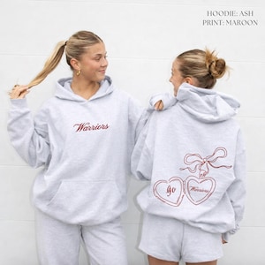 Puede incluir: Sudadera con capucha gris claro con la palabra "Warriors" en escritura granate en la parte delantera. La parte trasera presenta un dise&ntilde;o de medall&oacute;n en forma de coraz&oacute;n granate con "Go Warriors". Parte de un conjunto a juego.