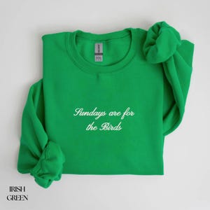K&ouml;nnte beinhalten: Irisch gr&uuml;nes Sweatshirt mit dem Text "Sundays are for the Birds" in Schreibschrift. Das lang&auml;rmlige Oberteil ist mit den &Auml;rmeln und einem Scrunchie oben gefaltet. Das Sweatshirt ist aus einem weichen Material.