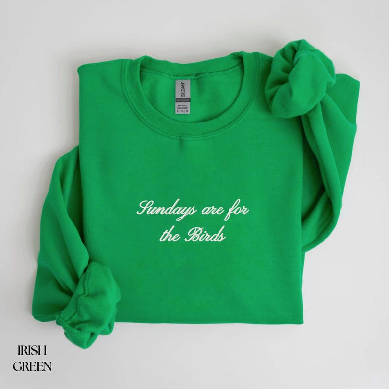 K&ouml;nnte beinhalten: Irisch gr&uuml;nes Sweatshirt mit dem Text "Sundays are for the Birds" in Schreibschrift. Das lang&auml;rmlige Oberteil ist mit den &Auml;rmeln und einem Scrunchie oben gefaltet. Das Sweatshirt ist aus einem weichen Material.