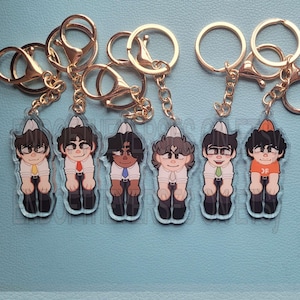 May include: Six colourful cartoon character keychains with gold key rings. Each keychain features a different character with a white hat and a different coloured shirt. The characters are standing with their hands at their sides.