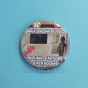 May include: A circular pin-back button featuring a beige-toned image of a figure standing in a room with the text "WHAT IF WE KISSED IN KANE PARSONS' BACKROOMS" in white letters with a black outline, accented by red heart and yellow emoji icons.