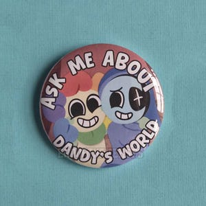Puede incluir: Una chapa redonda con una colorida ilustración de dibujos animados de dos personajes con ojos grandes y sonrisas amplias. El texto "ASK ME ABOUT DANDY'S WORLD" está impreso en letras mayúsculas blancas a lo largo de los bordes curvos.