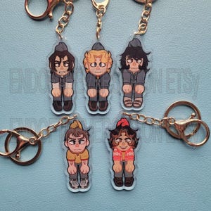 Peut inclure: Cinq porte-clés de personnages de dessins animés colorés avec des chaînes dorées. Les personnages portent des tenues différentes et ont des coiffures différentes. Les porte-clés sont en acrylique transparent et mesurent environ 5 cm de haut.