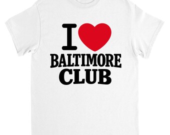 Puede incluir: Camiseta blanca con el texto "I ♥ BALTIMORE CLUB" en negro y rojo. La "I" es negra, el corazón es rojo y las palabras "BALTIMORE CLUB" están en negrita negra. La camiseta es de cuello redondo.
