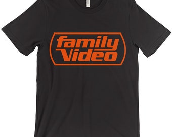 Puede incluir: Camiseta negra con un logotipo naranja "family video" en estilo retro.