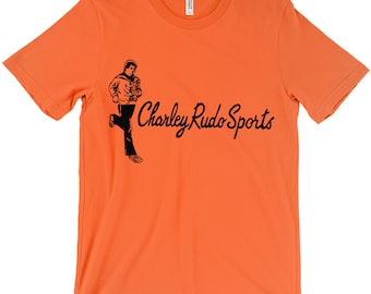 Puede incluir: Camiseta naranja con una ilustración negra de una persona corriendo y el texto "Charley Rudo Sports" en una fuente cursiva.