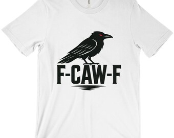 Puede incluir: Camiseta blanca con un diseño de cuervo negro con ojos rojos y el texto "F-CAW-F". El diseño gráfico es audaz y llamativo. La camiseta está hecha de un material suave y cómodo, ideal para el uso diario.