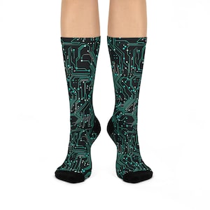 May include: A pair of knee-high socks featuring a black background with a teal circuit board design. The socks have black toes and heels. The design resembles the internal components of a computer.