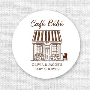 May include: A round white sticker with a brown illustration of a cafe, tables, and a baby carriage. The text "Café Bébé" is above the cafe, and "OLIVIA & JACOB'S BABY SHOWER" is below.