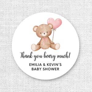 Puede incluir: Una pegatina redonda blanca con un oso de peluche marrón que sostiene un globo rosa en forma de corazón. El texto "Thank you beary much!" está escrito en letra cursiva negra. Debajo del texto está "Emilia & Kevin's Baby Shower" en letra negra.