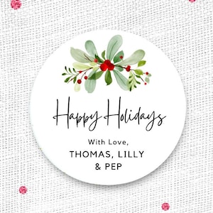 May include: A white circular sticker with the text "Happy Holidays" in black script. The sticker is decorated with a watercolor design of green leaves and red berries. The text "With Love, THOMAS, LILLY & PEP" is also included.