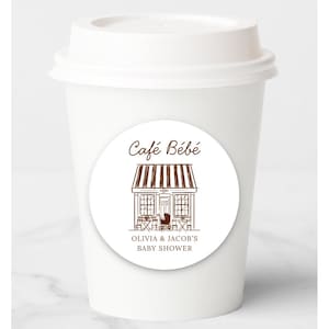 Puede incluir: Una taza de caf&eacute; de papel blanco con tapa blanca. Una pegatina redonda en la taza presenta una ilustraci&oacute;n marr&oacute;n de un caf&eacute; con el texto "Caf&eacute; B&eacute;b&eacute;" y "OLIVIA & JACOB'S BABY SHOWER".