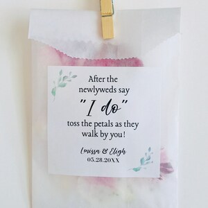 Puede incluir: Una bolsa de papel blanca con un dise&ntilde;o de acuarela rosa y verde. La bolsa tiene una etiqueta que dice "Despu&eacute;s de que los reci&eacute;n casados digan "S&iacute;, quiero" tira los p&eacute;talos mientras pasan por ti!" y "Lenissa & Eligh 05.28.20XX".