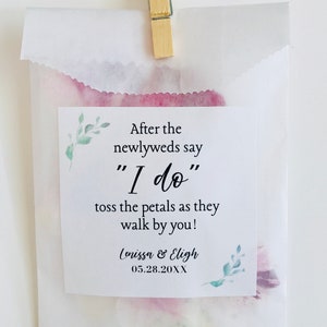 Puede incluir: Una bolsa de papel blanca con un dise&ntilde;o floral y una tarjeta impresa que dice "Despu&eacute;s de que los reci&eacute;n casados digan "S&iacute;, quiero" tira los p&eacute;talos mientras pasan por ti!" Lenissa & Eligh 05.28.20XX"