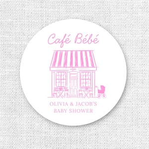 Puede incluir: Una pegatina circular blanca con texto e ilustraciones rosas. El texto "Caf&eacute; B&eacute;b&eacute;" est&aacute; encima de un dibujo de un caf&eacute; con un toldo a rayas. Debajo est&aacute; el texto "OLIVIA & JACOB'S BABY SHOWER".