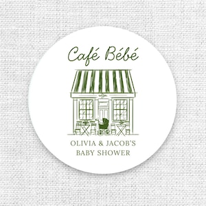 Puede incluir: Una pegatina circular blanca con una ilustraci&oacute;n verde de un caf&eacute;, un toldo y texto. El texto dice "Caf&eacute; B&eacute;b&eacute;" encima de la ilustraci&oacute;n del caf&eacute; y "OLIVIA & JACOB'S BABY SHOWER" debajo.
