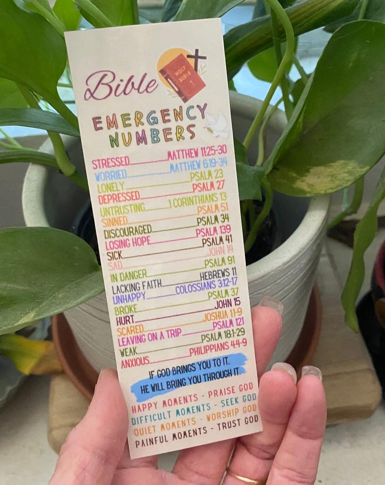 May include: A bookmark with the words "Bible Emergency Numbers" and a list of Bible verses for various emotional states. The bookmark has a cross and a small illustration of a book. The bottom of the bookmark has a blue banner with a quote.