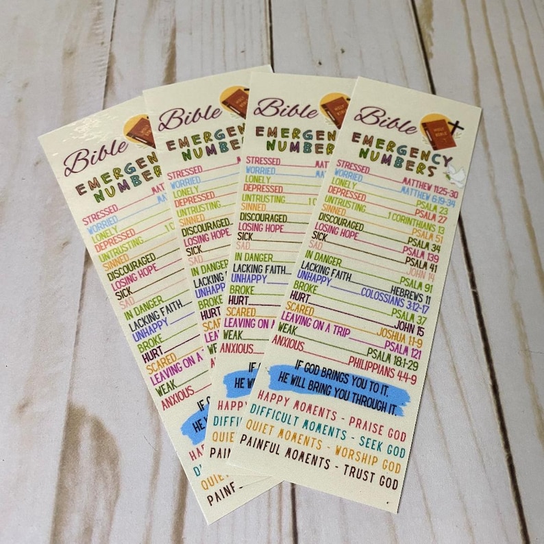 May include: Four Bible Emergency Number bookmarks. Each bookmark features a list of emotional states and corresponding Bible verses. The bookmarks have a cream background with text in various colors, including yellow, blue, and brown. The top of each bookmark has the word "Bible" and a small illustration.