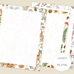 May include: Two sheets of stationery paper featuring woodland illustrations. One sheet is lined and the other is blank. Both feature borders with foxes, a rabbit, a deer, mushrooms, acorns, berries, and autumn leaves. A circular label reads LINED + BLANK.