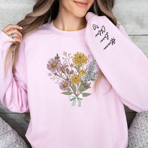 a woman wearing a pink sweatshirt with flowers on it
