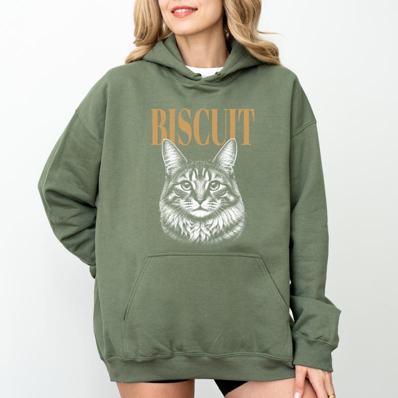 A woman wearing a green hoodie with a graphic of a cat and the word "Biscuit" printed on it.