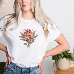 a woman with blonde hair wearing a white t - shirt with a rose on it