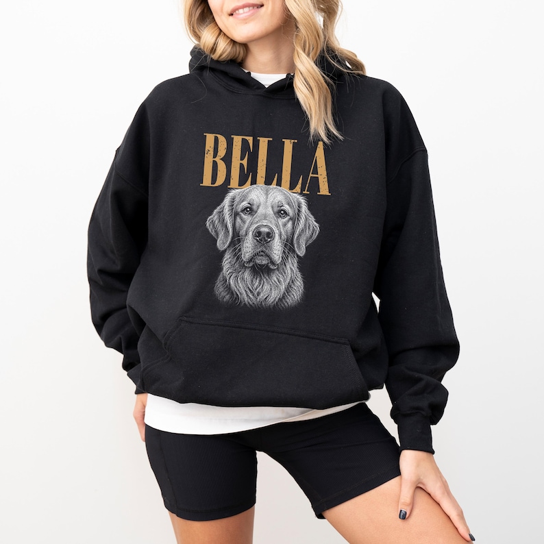 A woman wearing a black hoodie with a graphic of a dog's face and the name "Bella" printed on it.