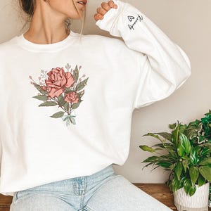 a woman wearing a white sweatshirt with a rose on it