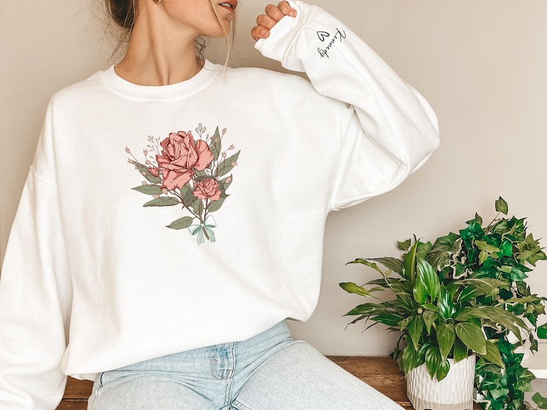 a woman wearing a white sweatshirt with a rose on it