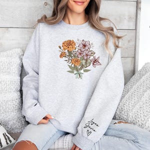 a woman sitting on a bed wearing a sweatshirt with flowers on it
