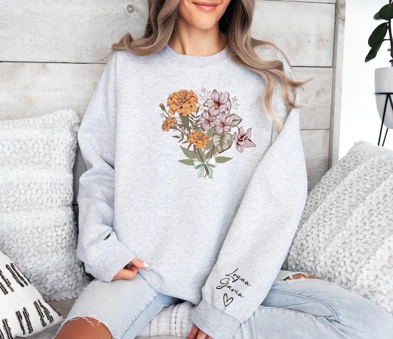 a woman sitting on a bed wearing a sweatshirt with flowers on it
