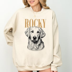 A woman wearing a beige sweatshirt with a graphic of Rocky, a dog, printed on it.