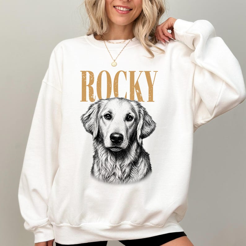 A woman wearing a white sweatshirt with a graphic of a dog's face and the word "ROCKY" printed on it.
