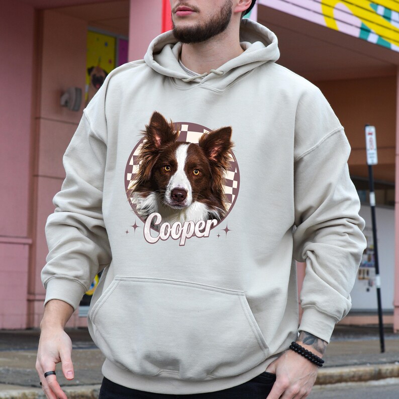 A man wearing a grey hoodie with a graphic of a dog's face and the name "Cooper" printed on it.