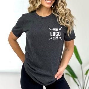 A woman with long, wavy blonde hair is wearing a gray t-shirt with a logo on it.